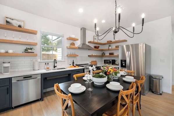 Una cocina moderna con comedor, electrodomésticos de acero inoxidable, estantes de madera y una araña.