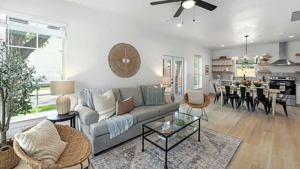 A modern living room with a grey sofa, a glass coffee table, and a dining area with a kitchen in the background.