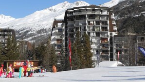 A multi-story hotel with balconies, set against a backdrop of snow-covered mountains. - 150m from ski slopes, 8th floor, view ski slopes, balcony, tv, ski locker, 38m², Serre Chevalier (La Salle-les-Alpes)