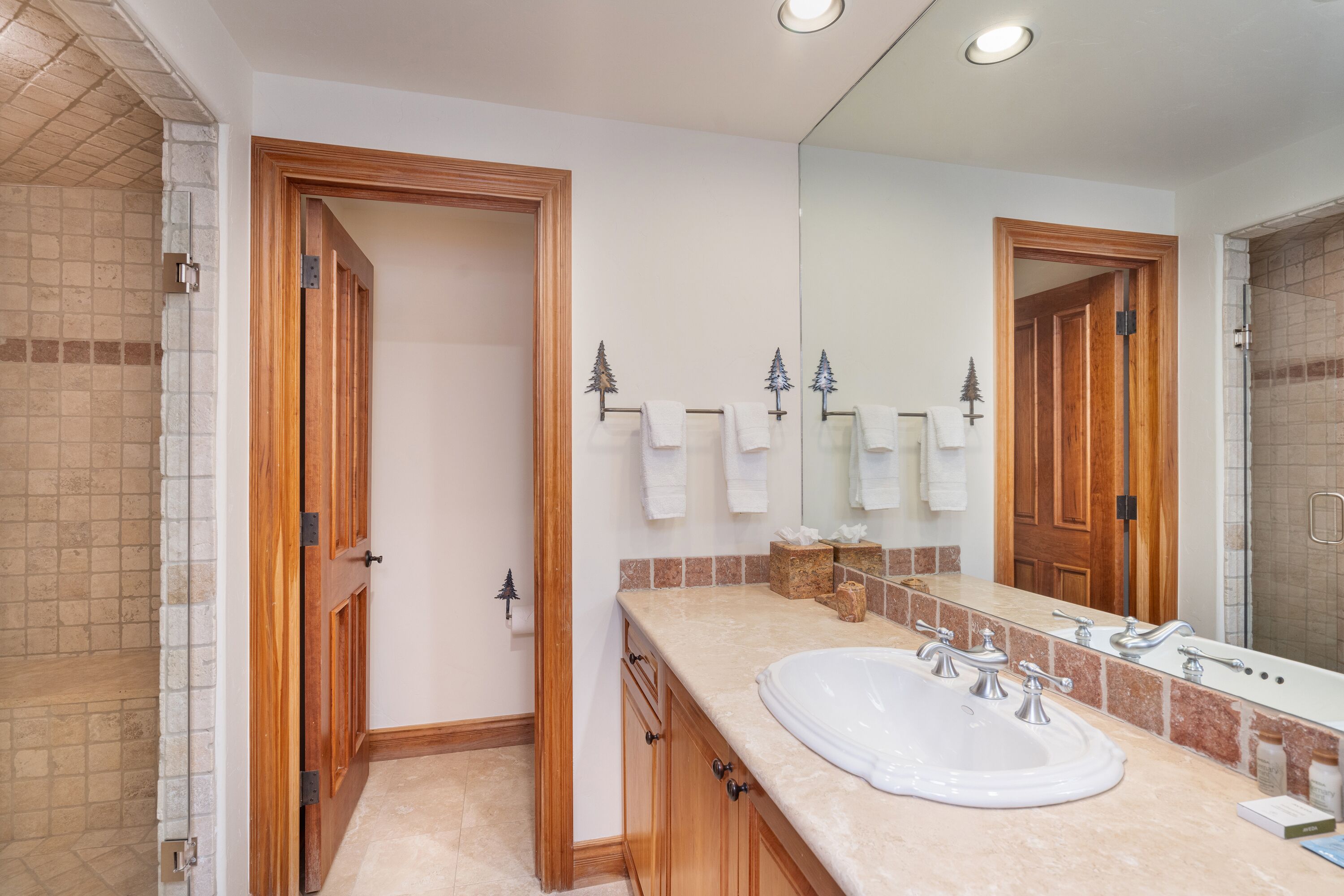 Un baño con un lavamanos amplio, armarios de madera, un espejo y una zona de ducha.