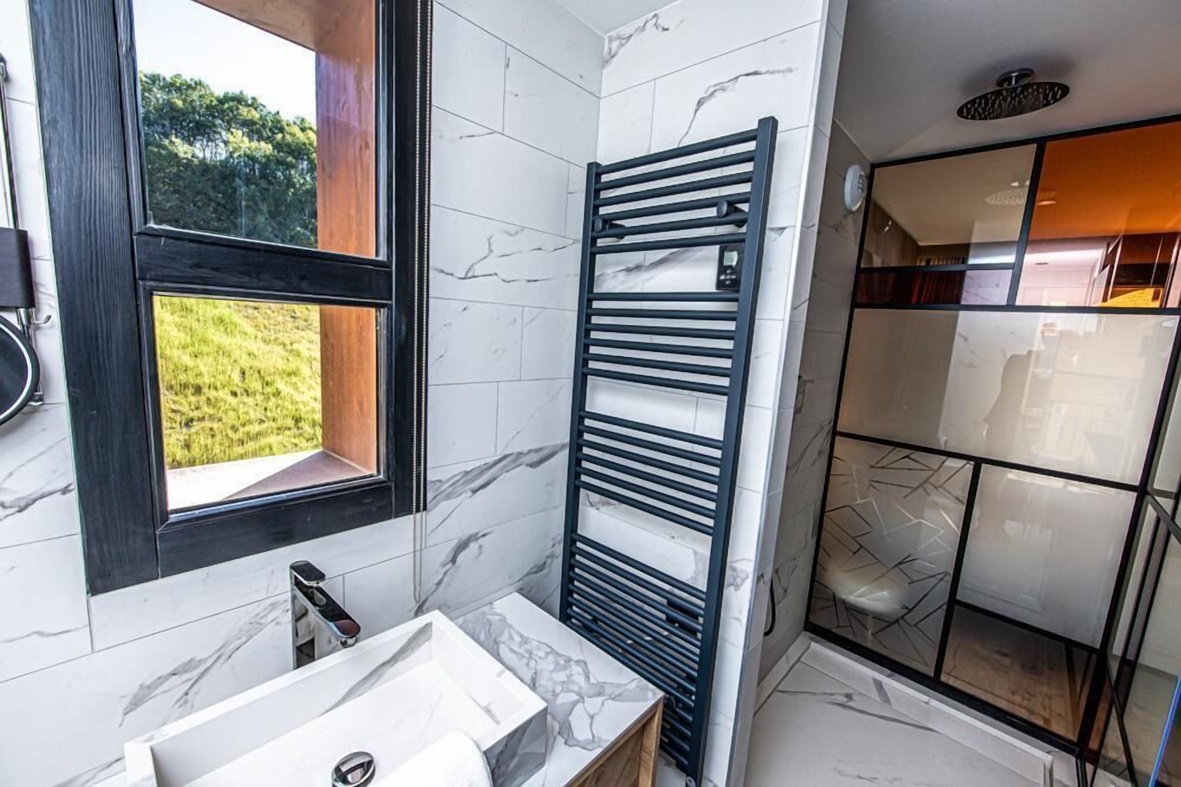 Un bagno moderno con un lavandino in marmo, un porta asciugamani nero e una cabina doccia in vetro.