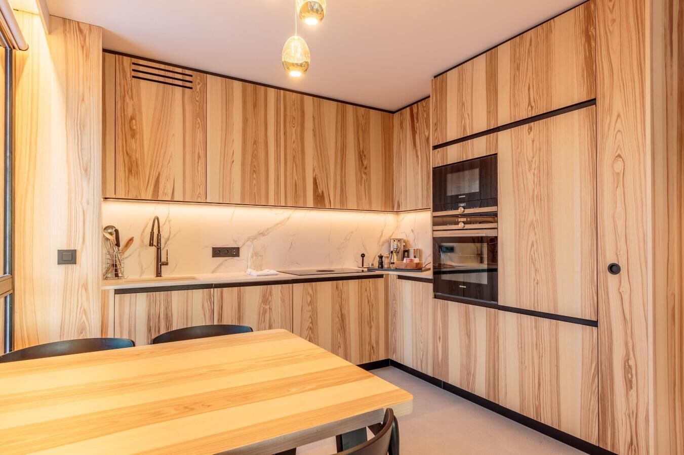A modern kitchen with wooden paneling, a marble backsplash, and built-in appliances.