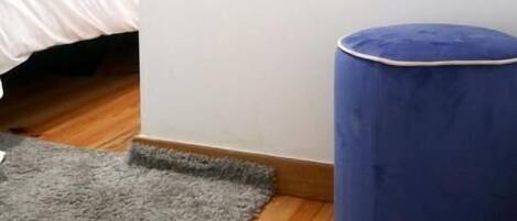 Un dormitorio con una cama, un espejo grande, un reposapiés azul y una alfombra gris.