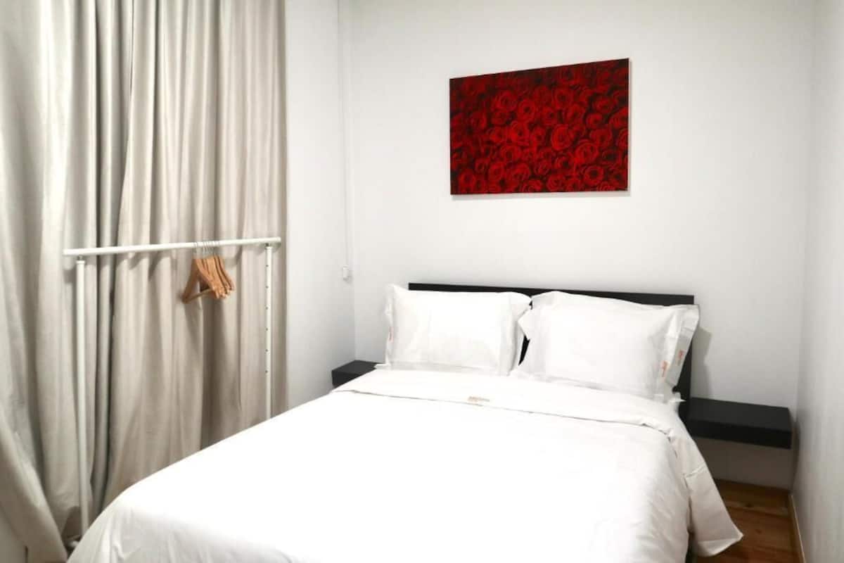 Un lit bien fait, avec une literie blanche et une œuvre d’art florale rouge accrochée au mur.