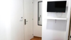 Une pièce avec un plancher en bois, une porte blanche, un téléviseur fixé au mur et un tabouret rouge.