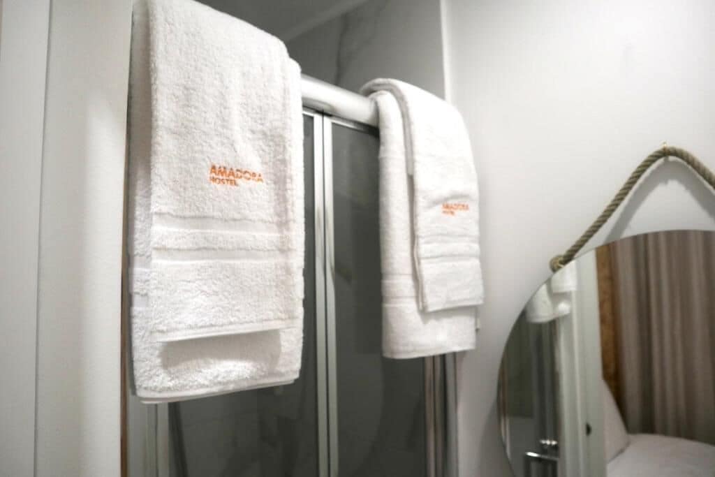 A bathroom with two white towels hanging on a towel rack, one with "AMAROS" embroidered on it.