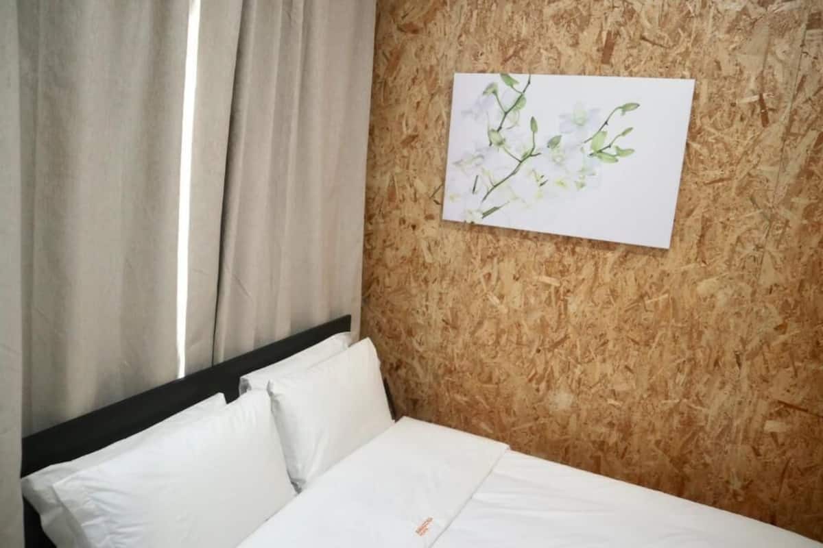 Une chambre d’hôtel avec un lit, du linge de lit blanc, un mur en bois et une œuvre d’art florale encadrée.