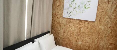 A hotel room with a bed, white linens, a wooden wall, and a framed floral artwork.