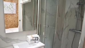 Une salle de bain avec une douche à parois de verre, un lavabo blanc et une serviette accrochée au mur.