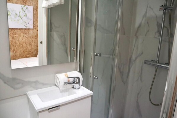 A bathroom with a glass shower enclosure, a white sink, and a towel hanging on the wall.