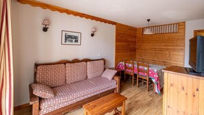 A cozy room with a patterned sofa, a dining table with chairs, a television, and a wooden wall. - 50m from ski slopes, 1st floor, view street, fitness, swimming pool, sauna, balcony, tv, ski locker (Les Orres)