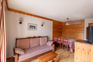 Una habitación acogedora con un sofá estampado, una mesa de comedor con sillas, un televisor y una pared de madera.