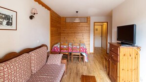 A cozy room with a wooden bench, a table with a floral tablecloth, a television on a wooden cabinet, and a framed picture on the wall. - 50m from ski slopes, 1st floor, view street, fitness, swimming pool, sauna, balcony, tv, ski locker (Les Orres)