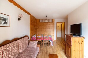 Una habitación acogedora con un banco de madera, una mesa con mantel floral, un televisor sobre un mueble de madera y un cuadro en la pared.