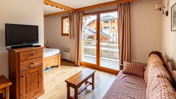 A cozy room with a wooden dresser, a bed, a bench, a sofa, and a television. - 50m from ski slopes, 1st floor, view street, fitness, swimming pool, sauna, balcony, tv, ski locker (Les Orres)