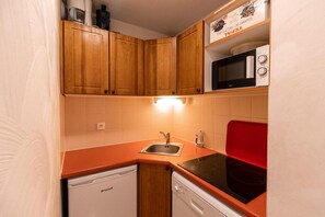 Una cocina compacta con armarios de madera, un fregadero, lavavajillas y microondas.