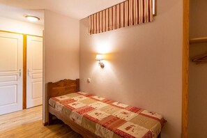 Un lit simple avec une couette, une lampe fixée au mur et une porte donnant sur une autre pièce.