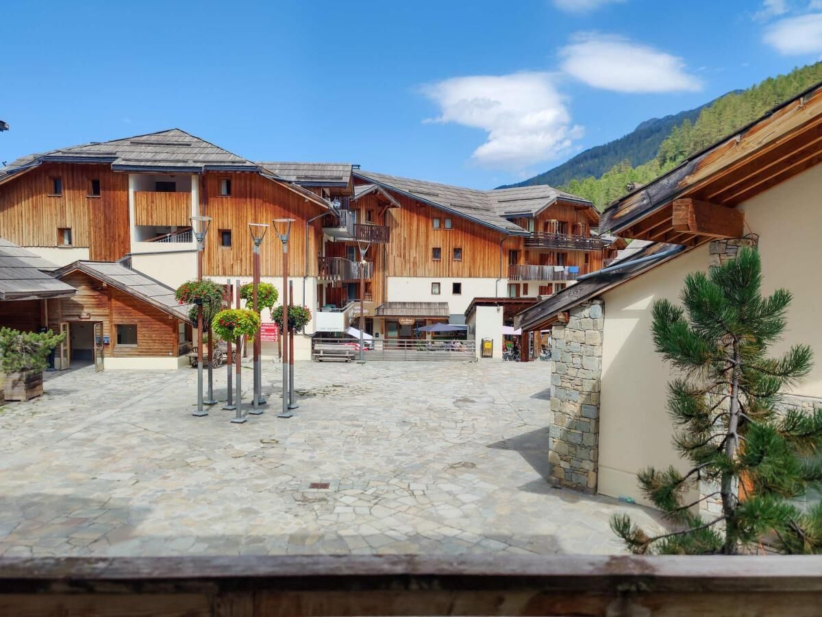 Un edificio de madera tradicional con un patio de piedra, balcones y un paisaje de montañas al fondo.