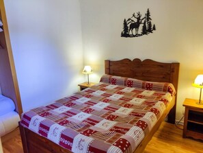 A bed with a patterned blanket, two bedside lamps, a wall decal of a moose and trees, and a wooden headboard.