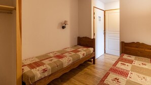 A small, single-bed room with a wooden headboard, a quilted bedspread, and a wall-mounted lamp. - 50m from ski slopes, 1st floor, view street, fitness, swimming pool, sauna, balcony, tv, ski locker (Les Orres)