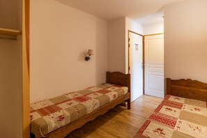 A small, single-bed room with a wooden headboard, a quilted bedspread, and a wall-mounted lamp. - 1st floor, view street, fitness, swimming pool, sauna, balcony, tv, ski locker, 38m², Les Orres (Les Orres)
