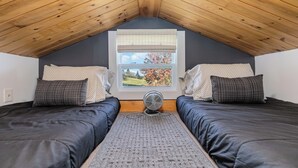 Una camera da letto con due letti, una finestra con persiane e un ventilatore.