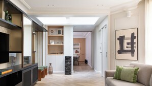 A modern living room with a sofa, a coffee table, and a TV. There is a hallway leading to a kitchen and a dining area. - HIGHSTAY - Luxury Serviced Apartments - Tuileries Garden (Paris)