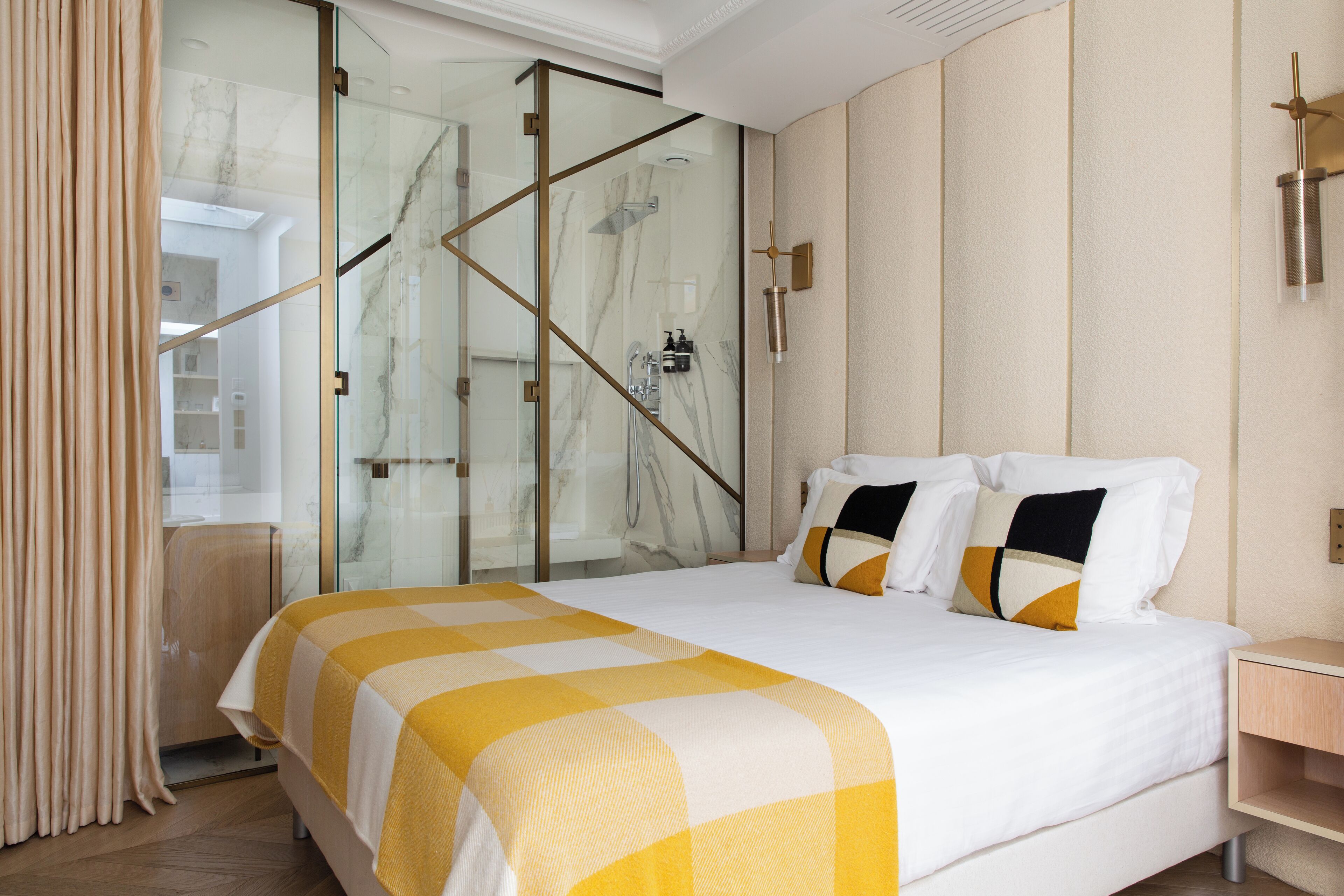 Habitación de hotel con una cama grande, cabina de ducha de vidrio y una mesita de noche de madera.