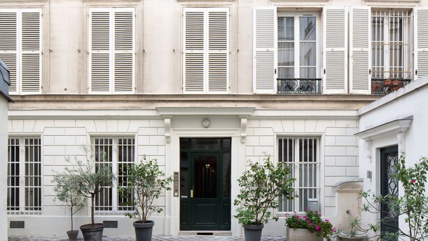 A building with a central entrance, multiple windows with shutters, and potted plants around the entrance. - HIGHSTAY - Luxury Serviced Apartments - Tuileries Garden (Paris)