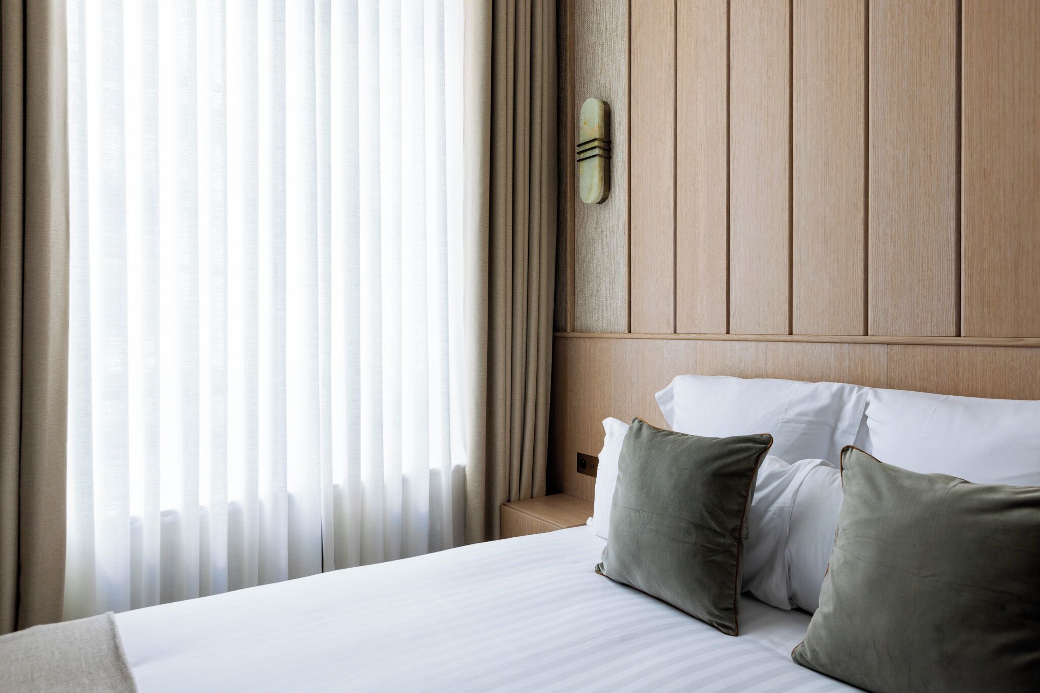 A hotel room with a large bed, a wooden headboard, and sheer curtains.