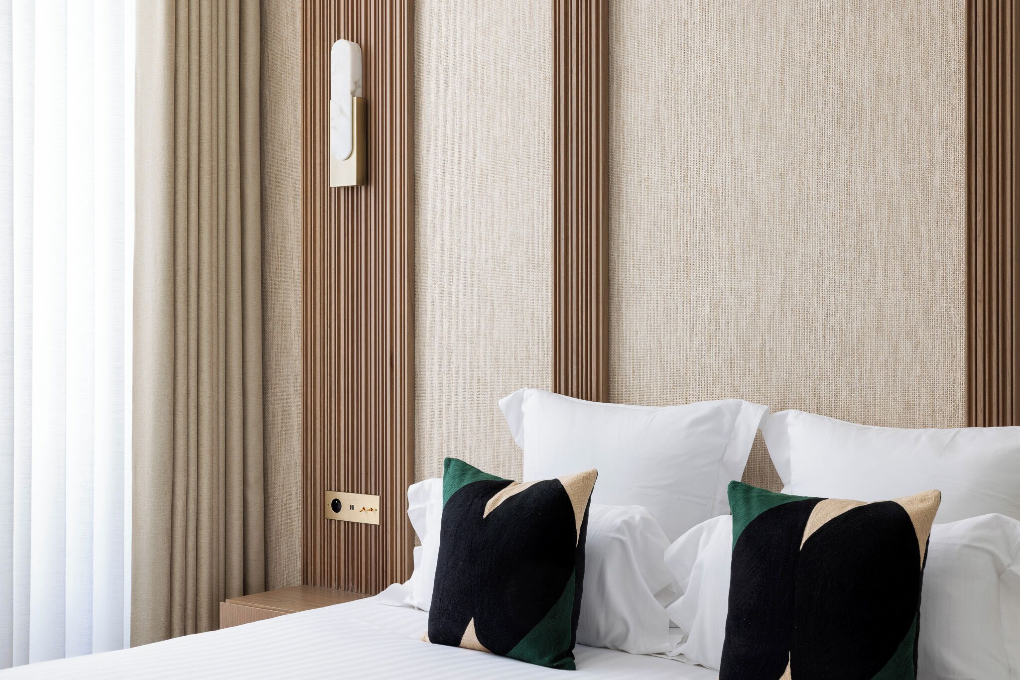 Ein Hotelzimmer mit einem Bett, zwei Kissen, einem Nachttisch und einem an der Wand befestigten Lichtschalter.