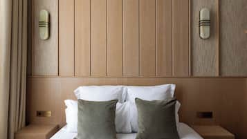 Cama bien hecha con sábanas blancas y dos almohadas verdes, cabecero de madera y mesitas de noche con lámparas.