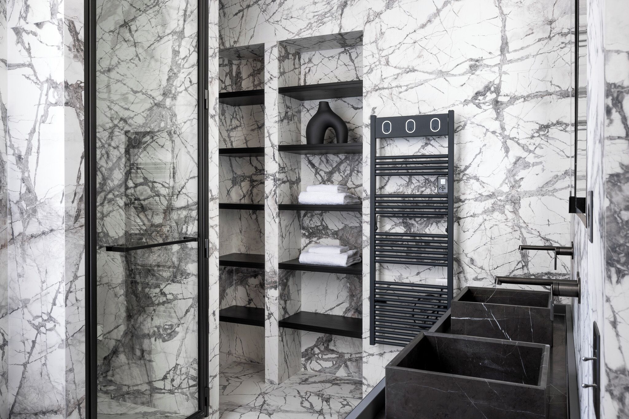 A bathroom with marble walls, black shelving units, and a towel rack.
