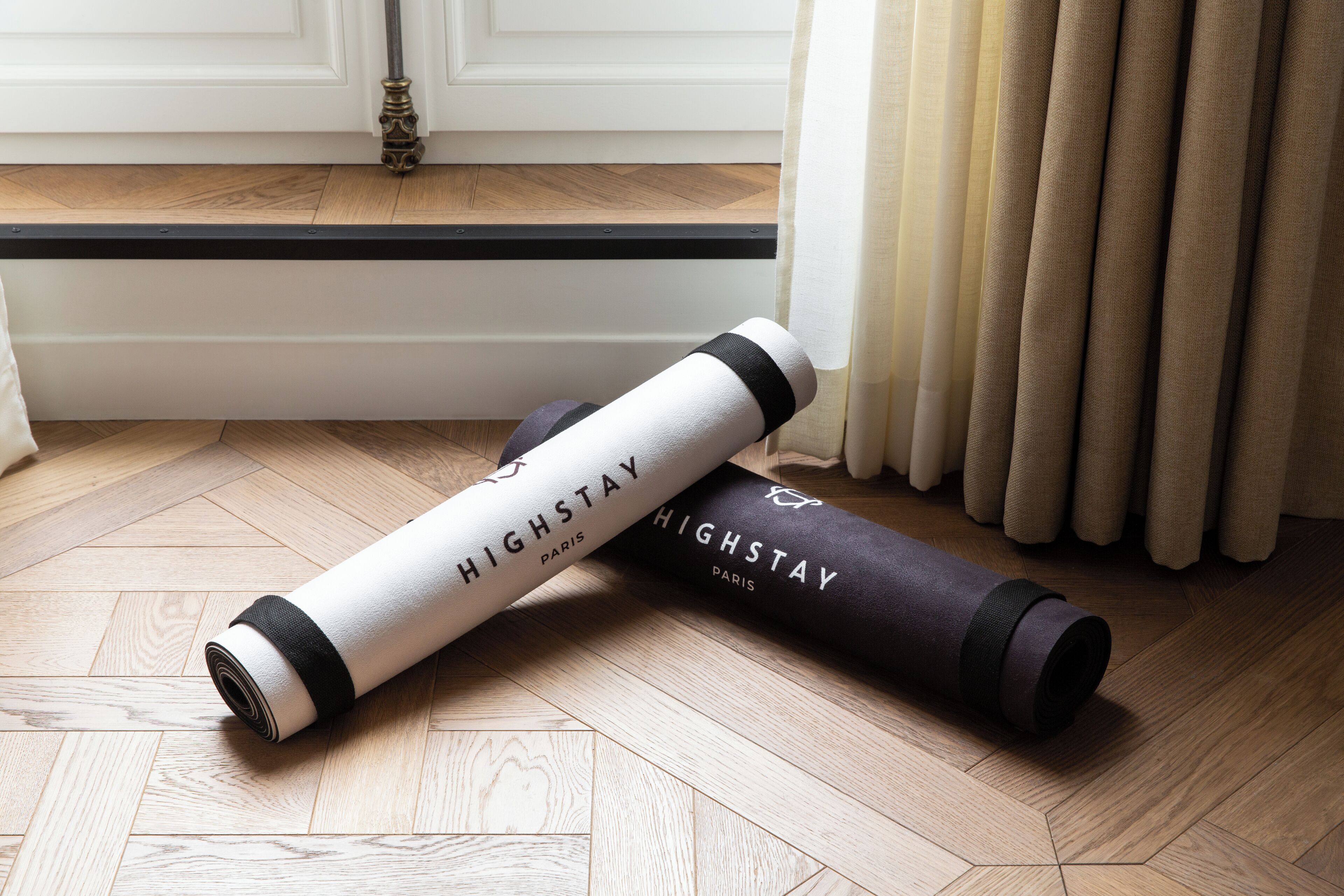 Two yoga mats labeled 'HIGHSTAY Paris' on a wooden floor near a window with curtains.