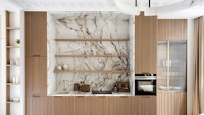 A modern kitchen with wooden cabinets, marble backsplash, and built-in shelves. - HIGHSTAY - Luxury Serviced Apartments - Le Marais (Paris)
