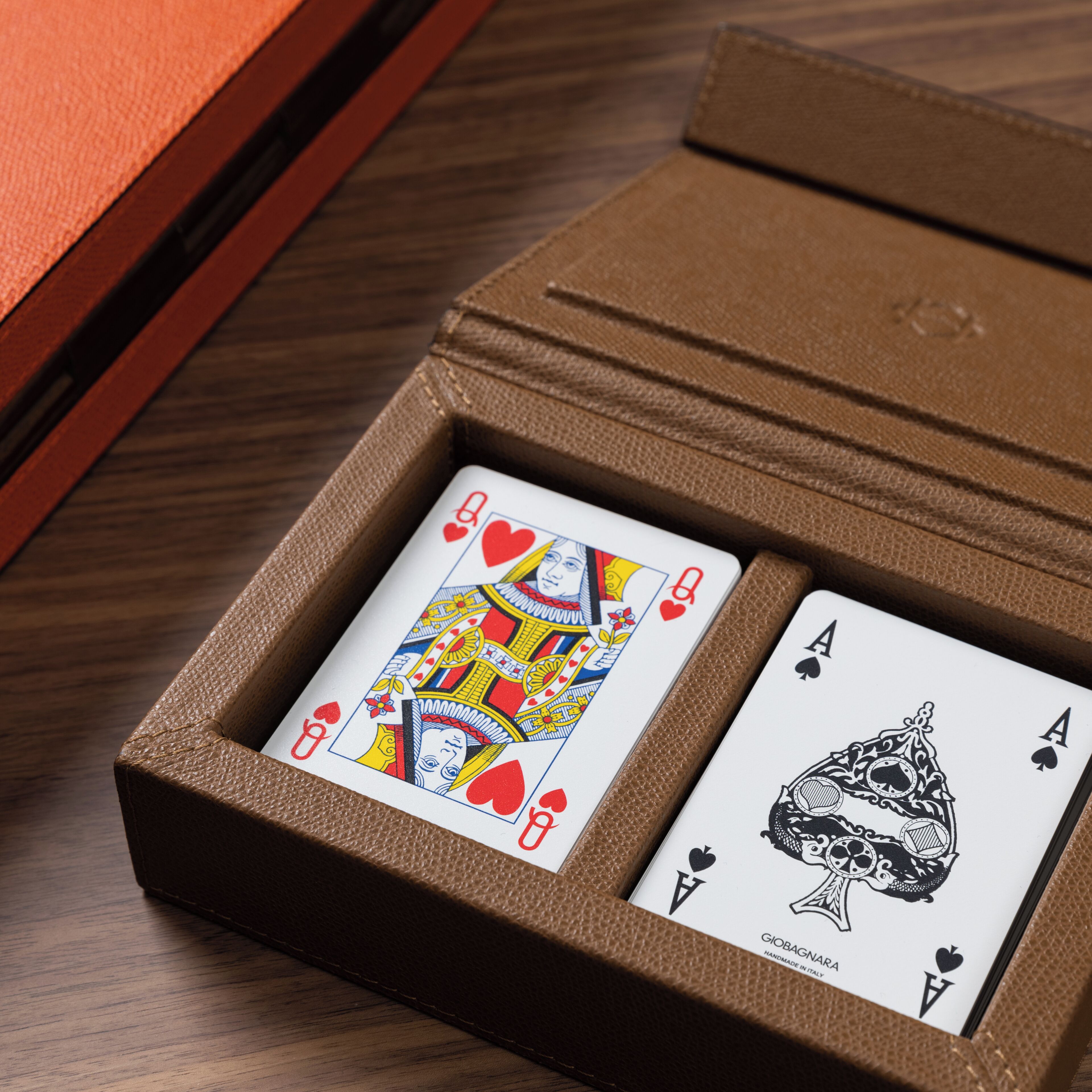 A brown leather card case with two playing cards, one Queen of Hearts and one Ace of Spades, on a wooden surface.