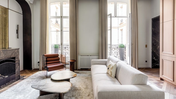 A spacious living room with a fireplace, a sofa, a coffee table, and a view of the city through large windows. - HIGHSTAY - Luxury Serviced Apartments - Le Marais (Paris)