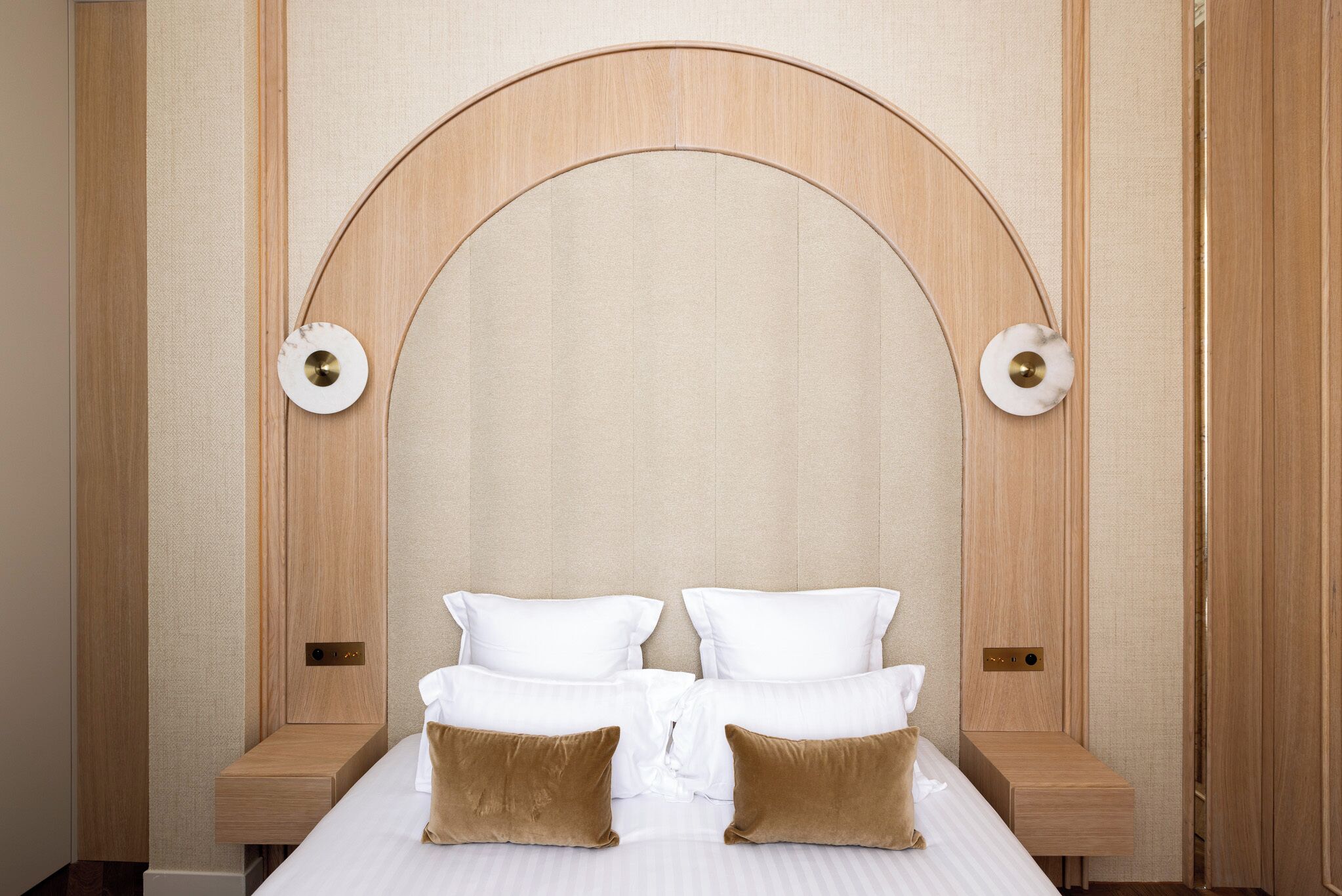 Una habitación de hotel con una cama grande, dos mesitas de noche y un cabecero de madera con un arco curvo.
