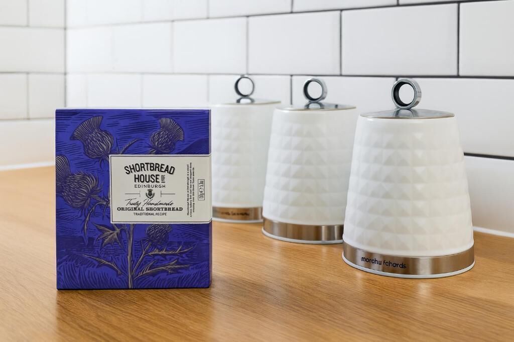 En ask med Shortbread House Edinburgh-kakor och tre vita keramikbehållare med handtag.
