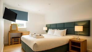 A neatly arranged hotel room with a bed, bedside lamps, a desk with a flat-screen TV, and a window. - Edinburgh Aparthotel (Edinburgh)