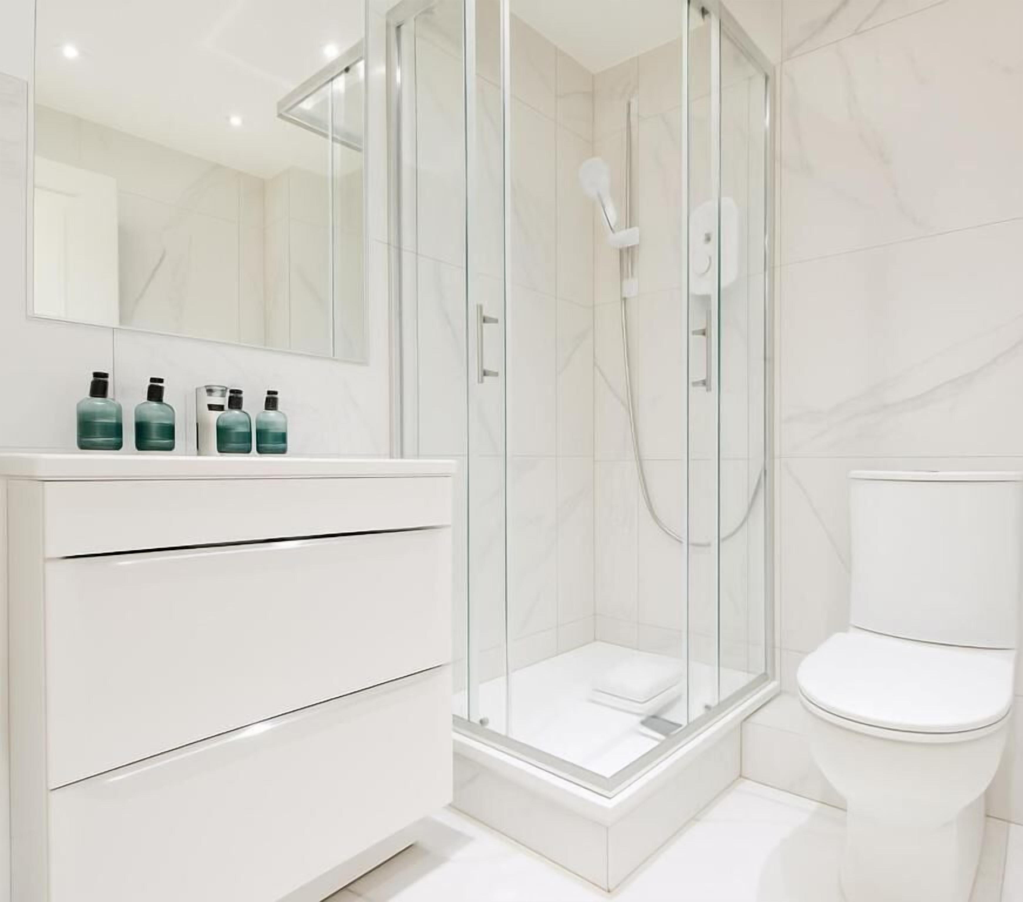 A modern bathroom with a glass-enclosed shower, a white toilet, and a vanity with drawers and a mirror.
