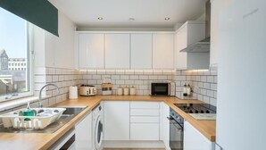 A modern kitchen with white cabinetry, a wooden countertop, a built-in oven, and a window providing a view of the city. - Edinburgh Aparthotel (Edinburgh)
