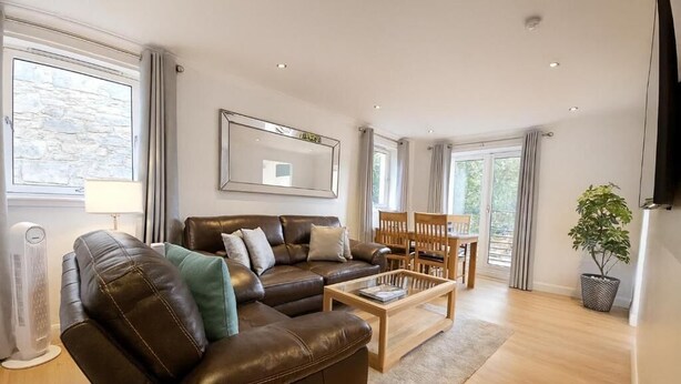 A modern living room with a leather sofa, wooden coffee table, and a dining area with a wooden table and chairs. - Edinburgh Aparthotel (Edinburgh)