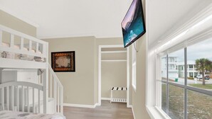 Ein Schlafzimmer mit Etagenbett, einem an der Wand befestigten Fernseher und einem Fenster mit Blick auf eine Straße.
