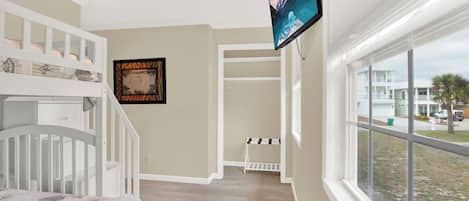 A bedroom with a bunk bed, a television mounted on the wall, and a window overlooking a street.