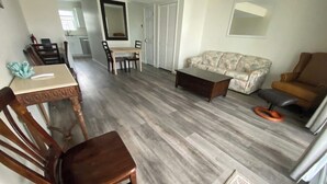 Ein Wohnzimmer mit einer Couch, einem Couchtisch, einem Esstisch mit Stühlen und einem gemusterten Teppich.