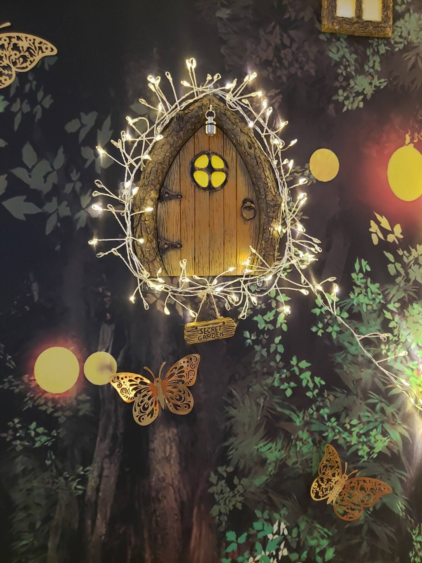 Una casa de madera con una puerta circular, rodeada de luces colgantes y un letrero que dice 'SECRET GARDEN'.