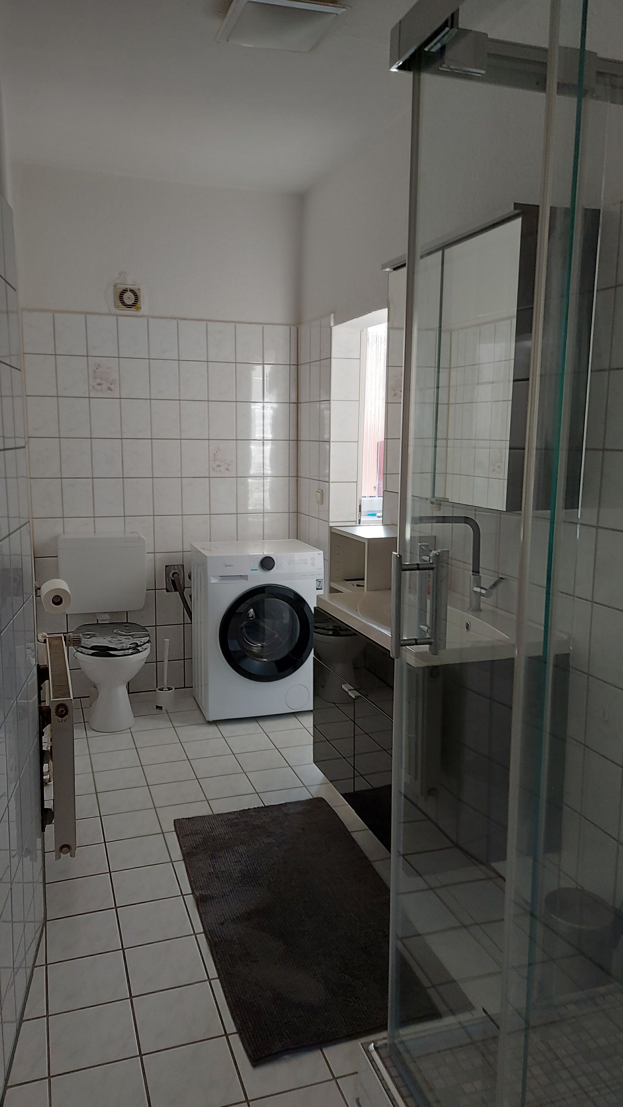 Un baño moderno con lavadora, inodoro y cabina de ducha de vidrio.