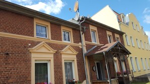 A two-story brick building with a yellow facade, multiple windows, and a small porch with a wooden railing.