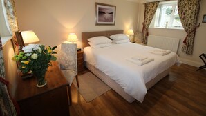 A hotel room with a large bed, bedside lamps, a nightstand, a vase of flowers, and a window with curtains. - Chaff House – Dog‑Friendly Family Cottage on Burradon Farm near coast (Cramlington)